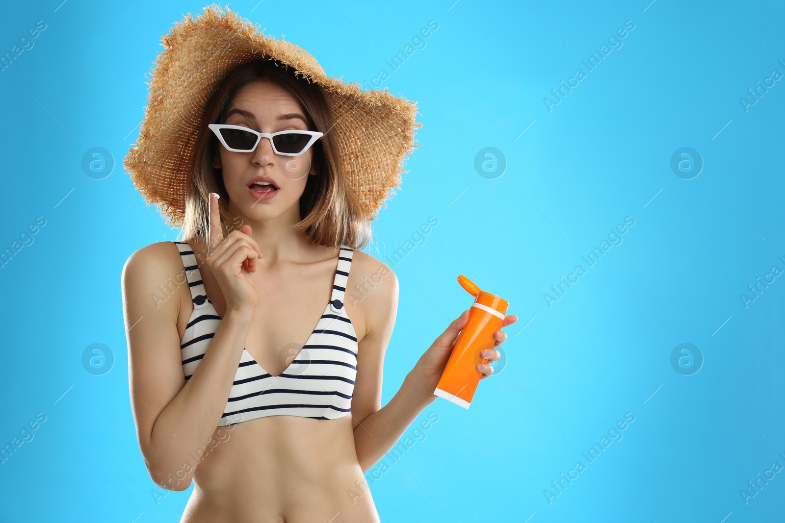 Photo of Emotional young woman applying sun protection cream on light blue background. Space for text