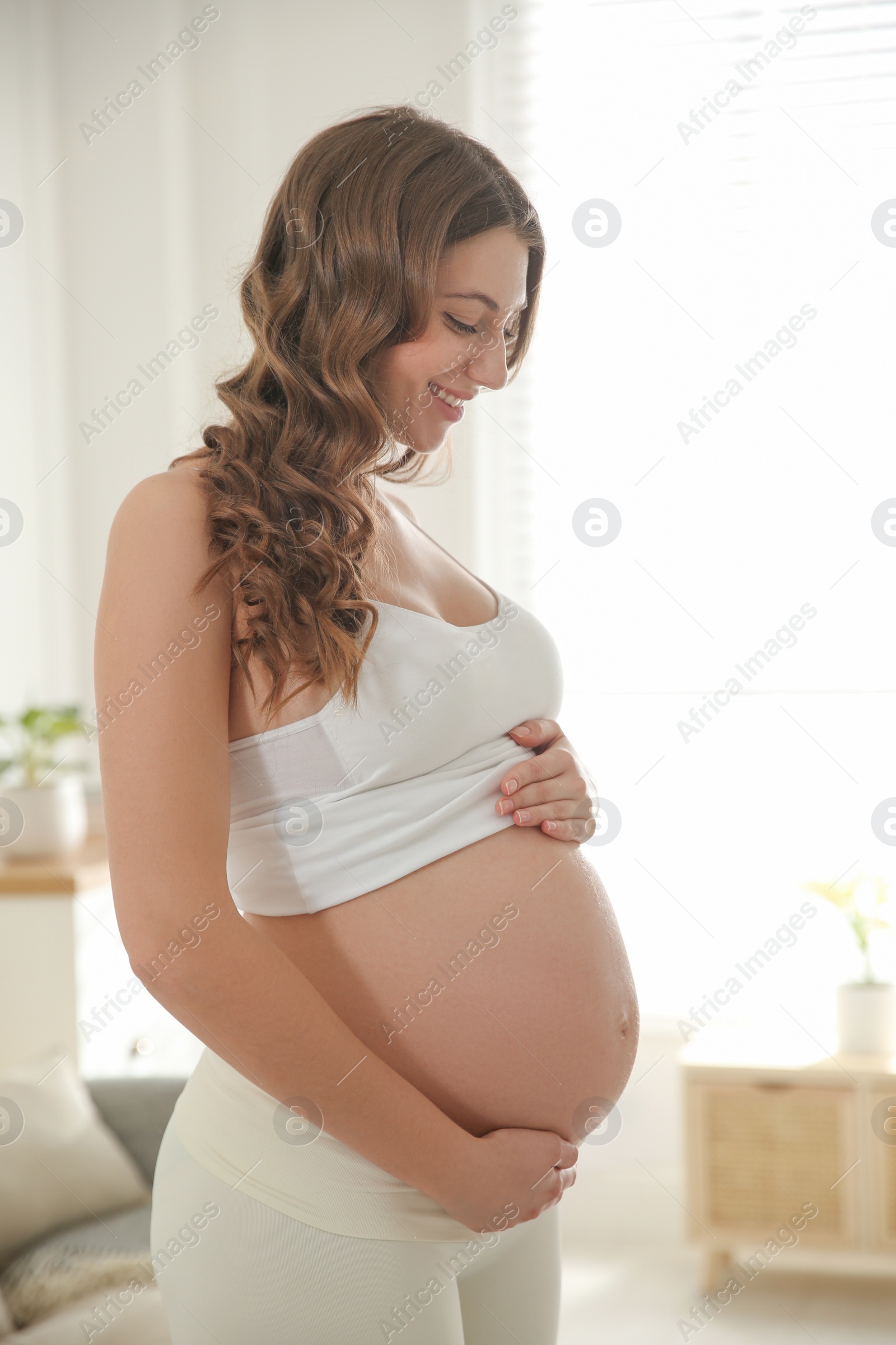 Photo of Happy pregnant woman touching her belly indoors