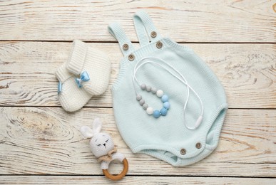 Cute knitted baby bodysuit, booties and toys on white wooden background, flat lay
