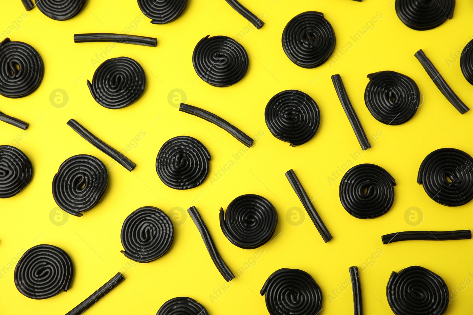 Photo of Tasty black liquorice candies on yellow background, flat lay