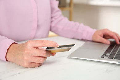 Online payment. Woman using credit card and laptop at white marble table indoors, closeup