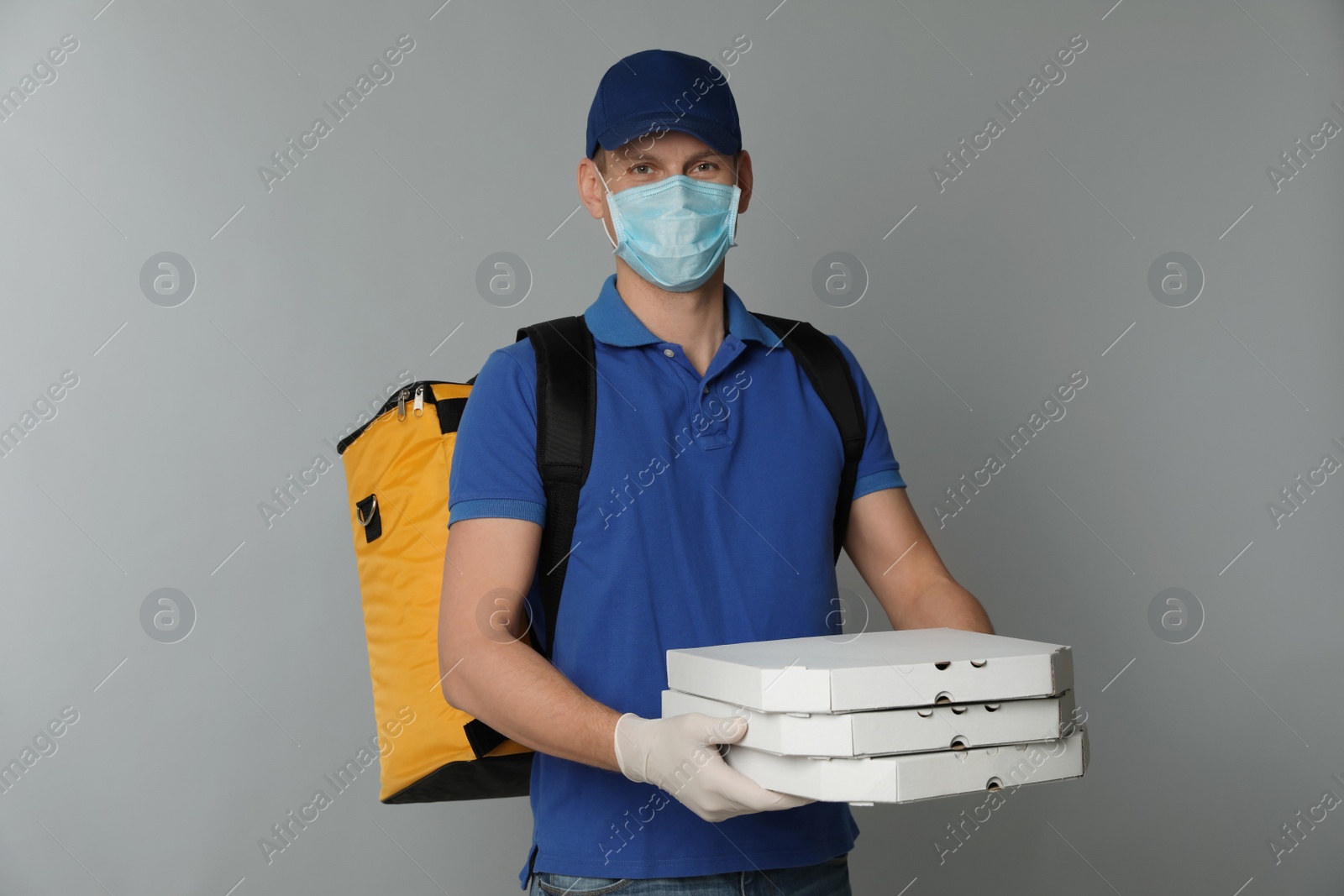 Photo of Courier in protective mask and gloves holding pizza boxes on light grey background. Food delivery service during coronavirus quarantine