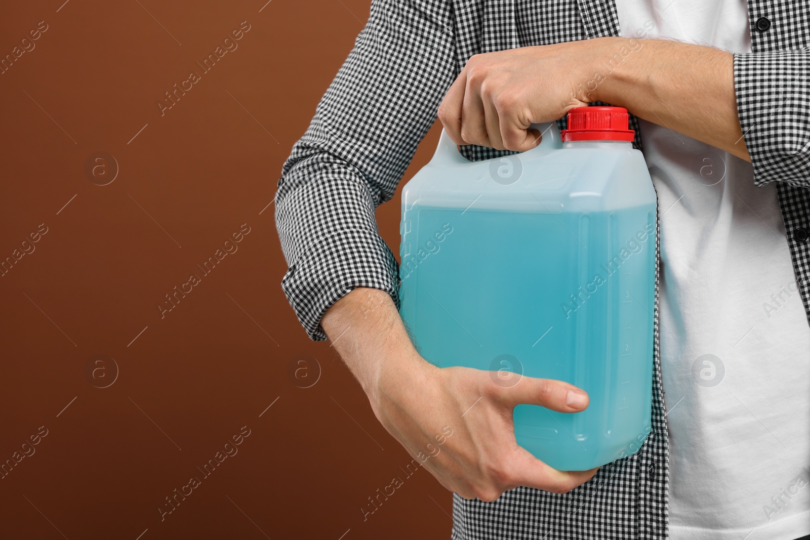 Photo of Man holding canister with blue liquid on brown background, closeup. Space for text