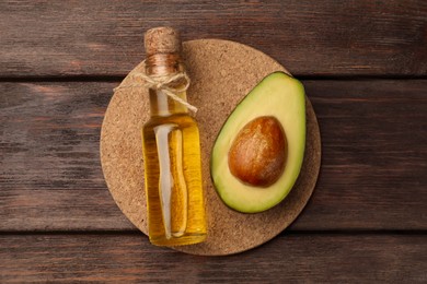 Photo of Glass bottlecooking oil and cut avocado on wooden table, top view