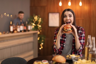 Young woman eating tasty burger in cafe