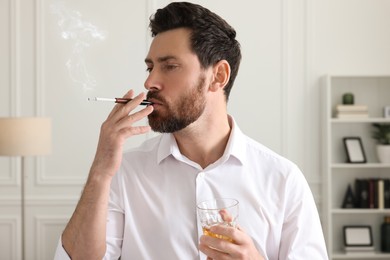 Man using cigarette holder for smoking and holding glass of whiskey in office