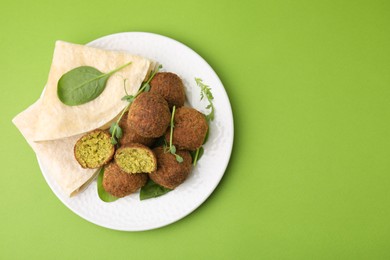 Photo of Delicious falafel balls, herbs and lavash on green background, top view. Space for text