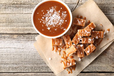 Photo of Caramel sauce with sea salt and yummy candies on wooden table, flat lay