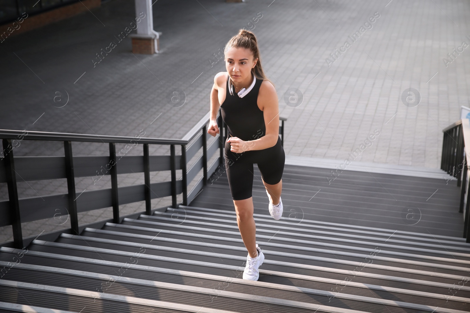 Photo of Young woman in sportswear with headphones running up stairs outdoors