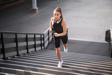 Photo of Young woman in sportswear with headphones running up stairs outdoors