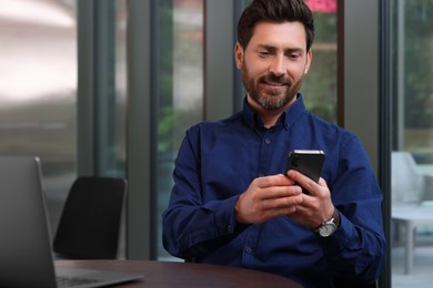 Photo of Handsome man using smartphone at table indoors