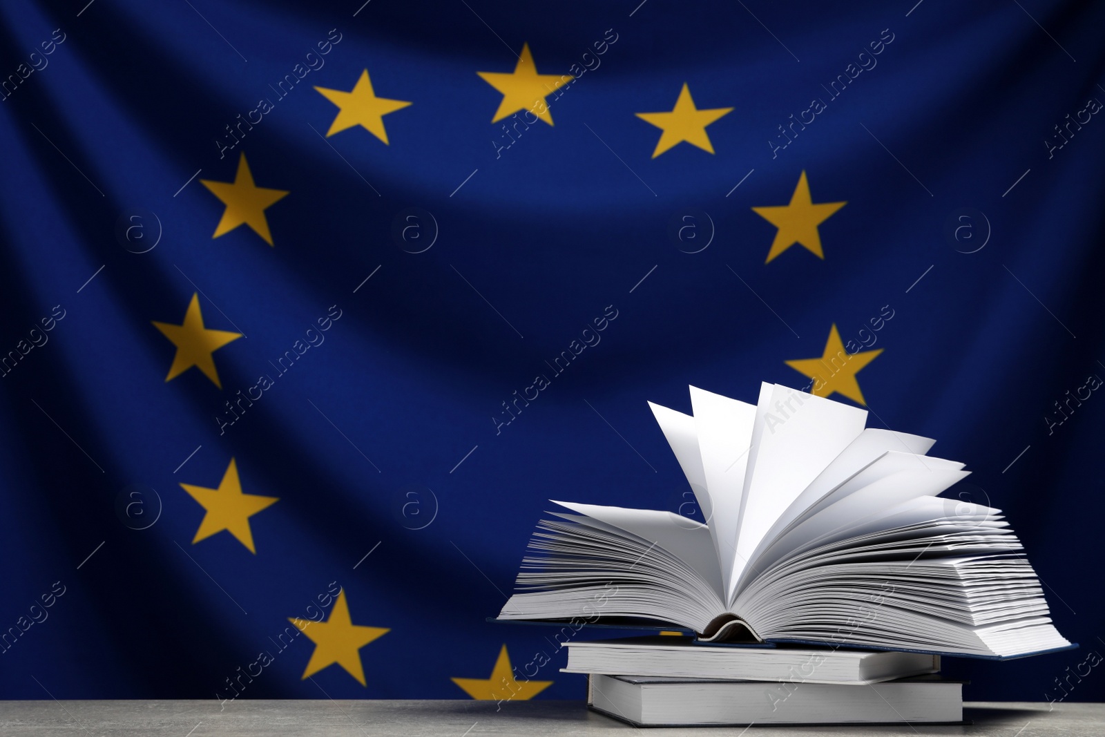 Photo of Books on light grey table against flag of European Union. Space for text