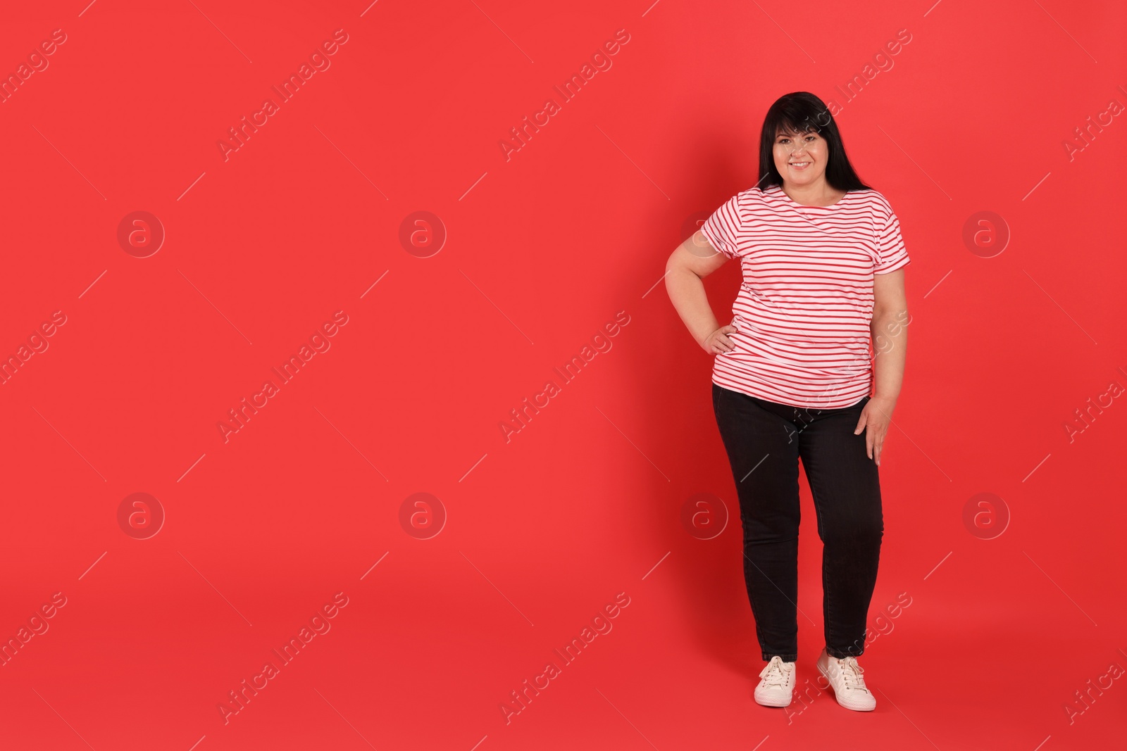 Photo of Beautiful overweight mature woman with charming smile on red background. Space for text