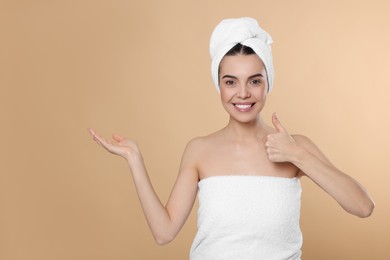 Young woman in towels showing thumb up on beige background, space for text. Spa treatment