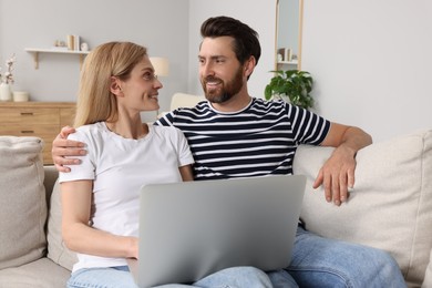 Happy couple with laptop on sofa at home