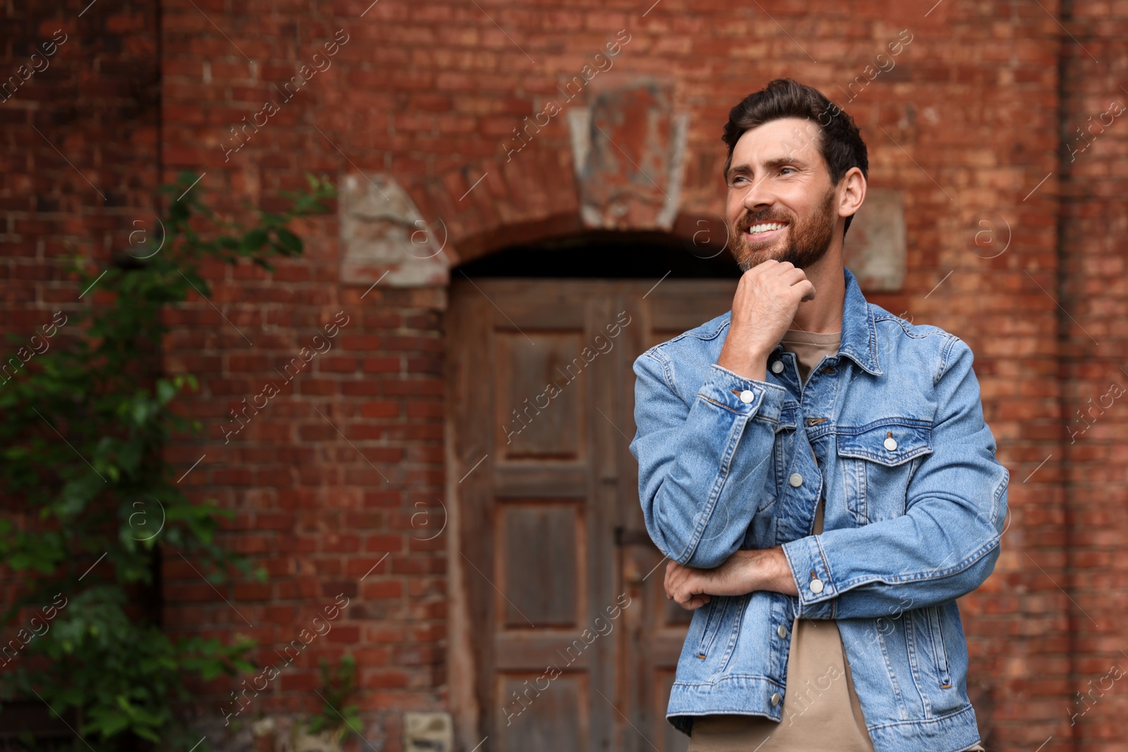 Photo of Smiling handsome bearded man looking away outdoors. Space for text