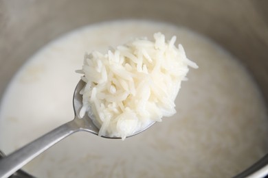 Photo of Spoon with tasty rice porridge over pot, closeup