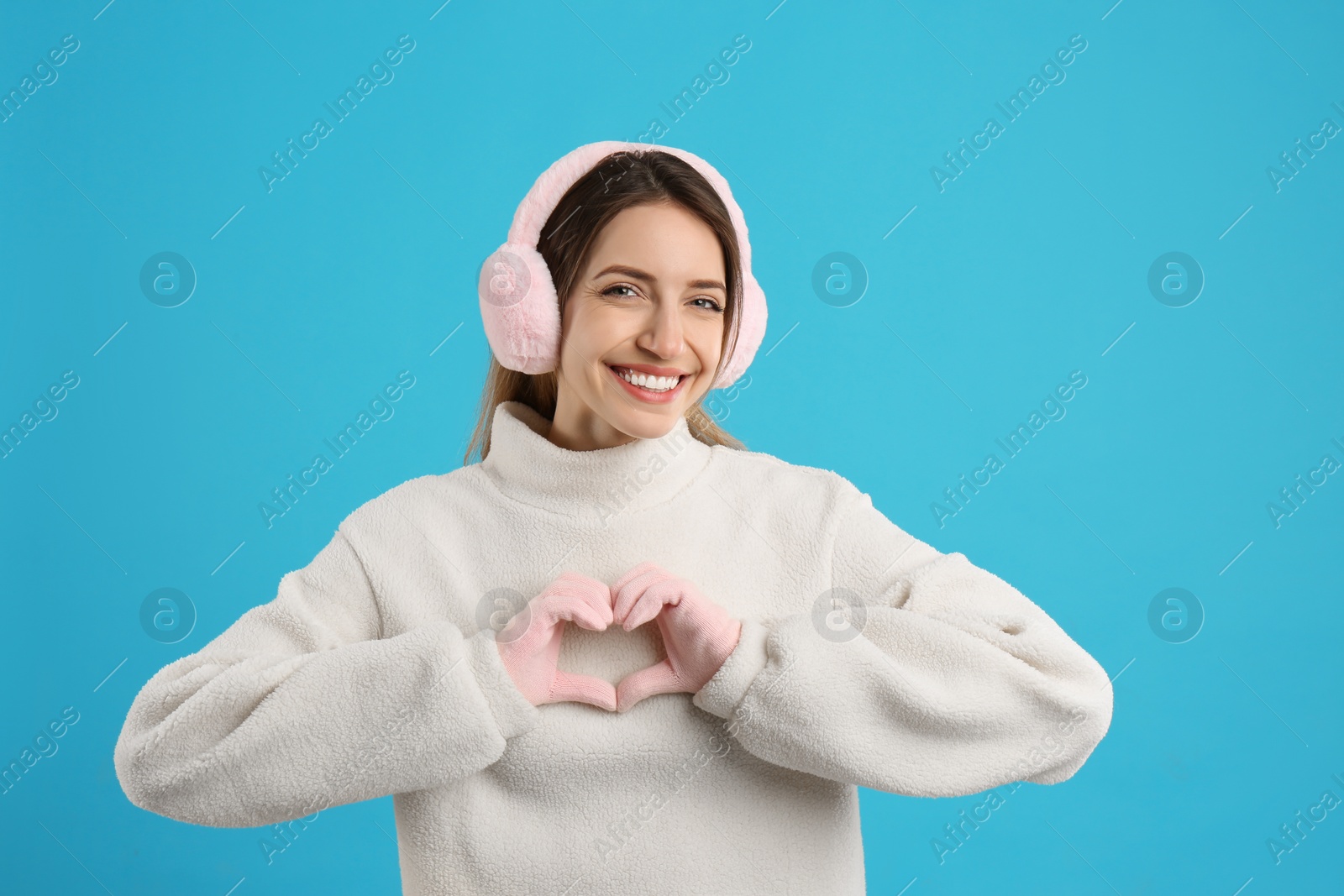 Photo of Happy woman wearing warm earmuffs on light blue background