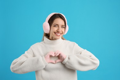 Happy woman wearing warm earmuffs on light blue background