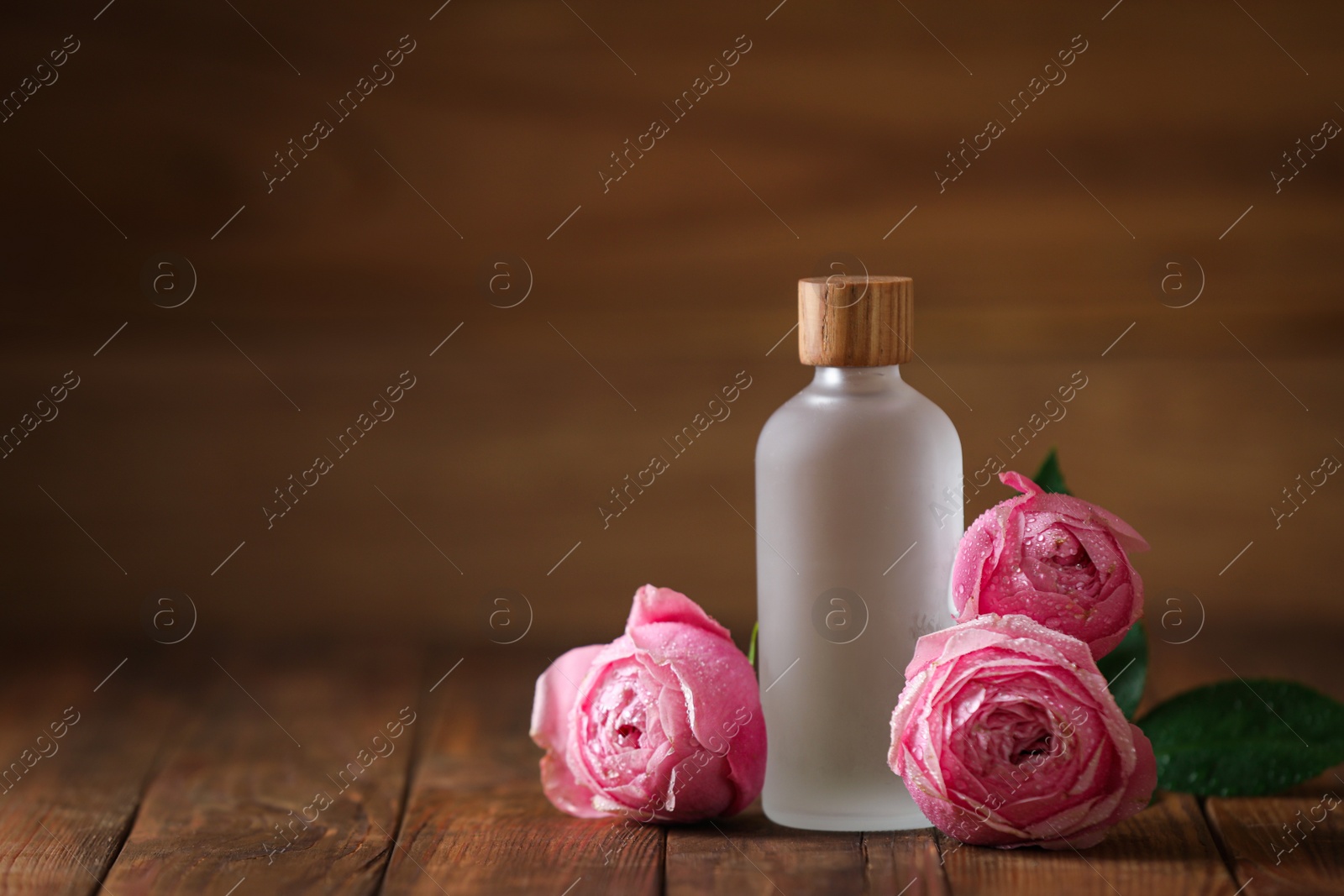 Photo of Bottle of essential rose oil and roses on wooden table. Space for text