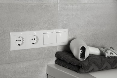 Photo of Power sockets, light switches on wall near table with hairdryer and towel indoors
