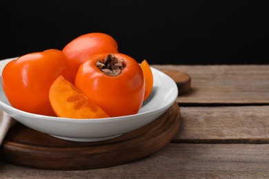 Photo of Delicious ripe persimmons on wooden table, closeup. Space for text