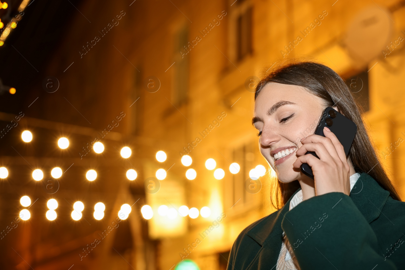 Photo of Smiling woman talking by smartphone on night city street. Space for text