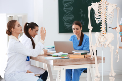Medical students studying human skeleton anatomy in classroom