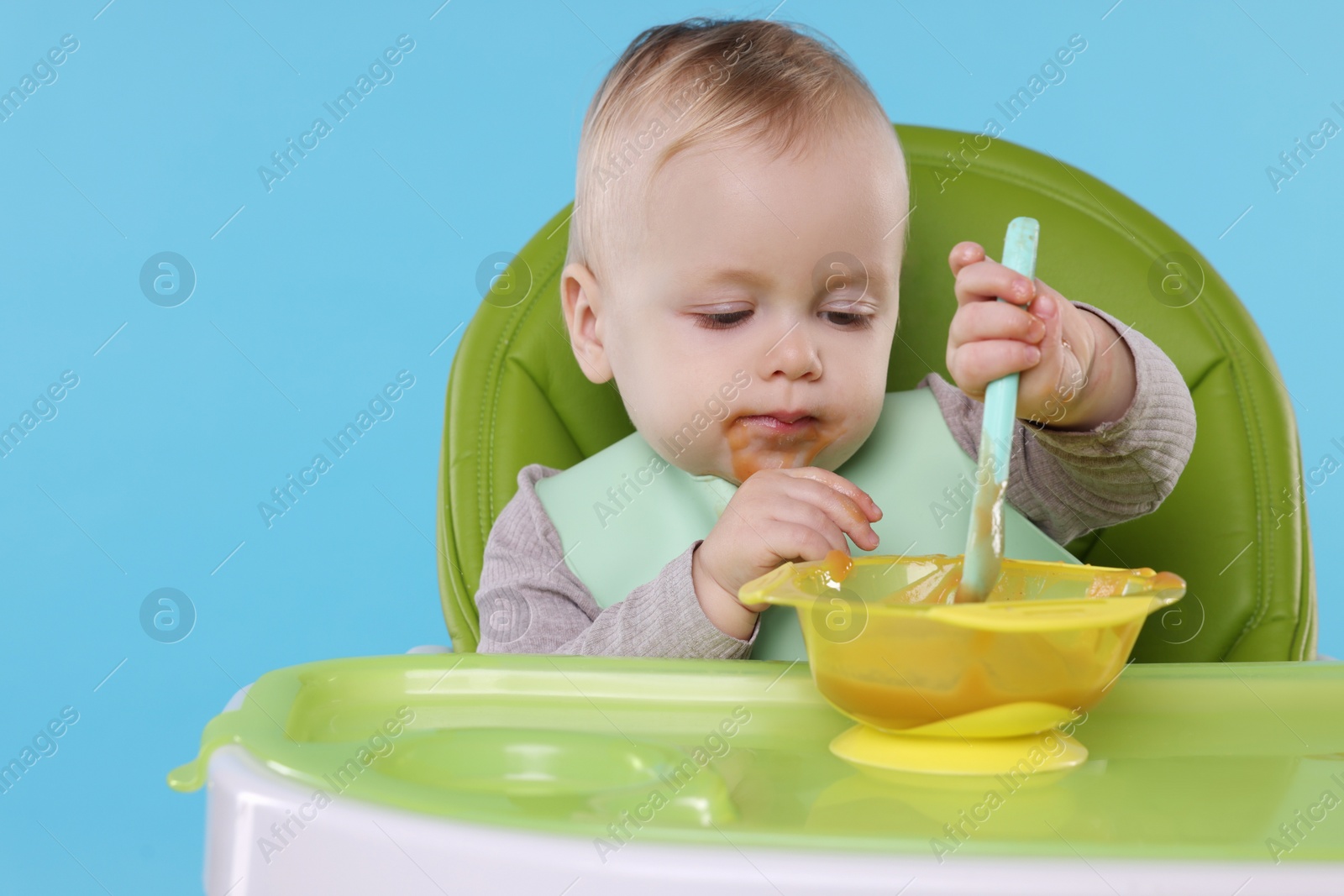 Photo of Cute little baby eating healthy food in high chair on light blue background