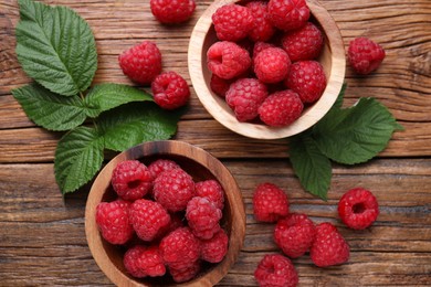 Tasty ripe raspberries and green leaves on wooden table, flat lay