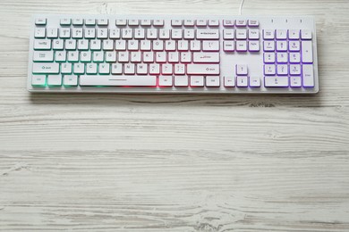 Photo of Modern RGB keyboard on white wooden table, top view. Space for text