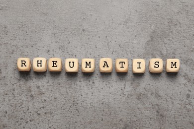 Word Rheumatism made of wooden cubes on light gray textured background, top view