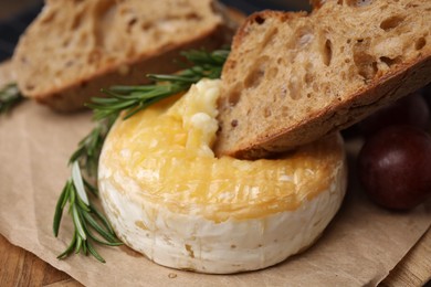 Photo of Dipping piece of bread into tasty baked camembert on table, closeup