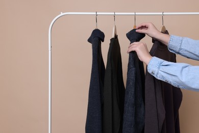 Photo of Woman taking sweater from rack on beige background, closeup