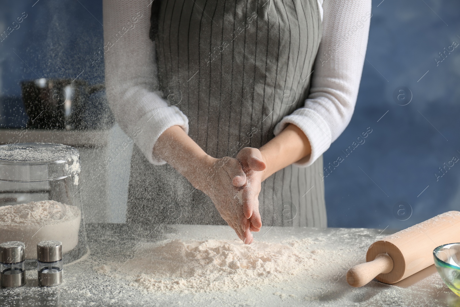Photo of Woman sprinkling flour over table in kitchen