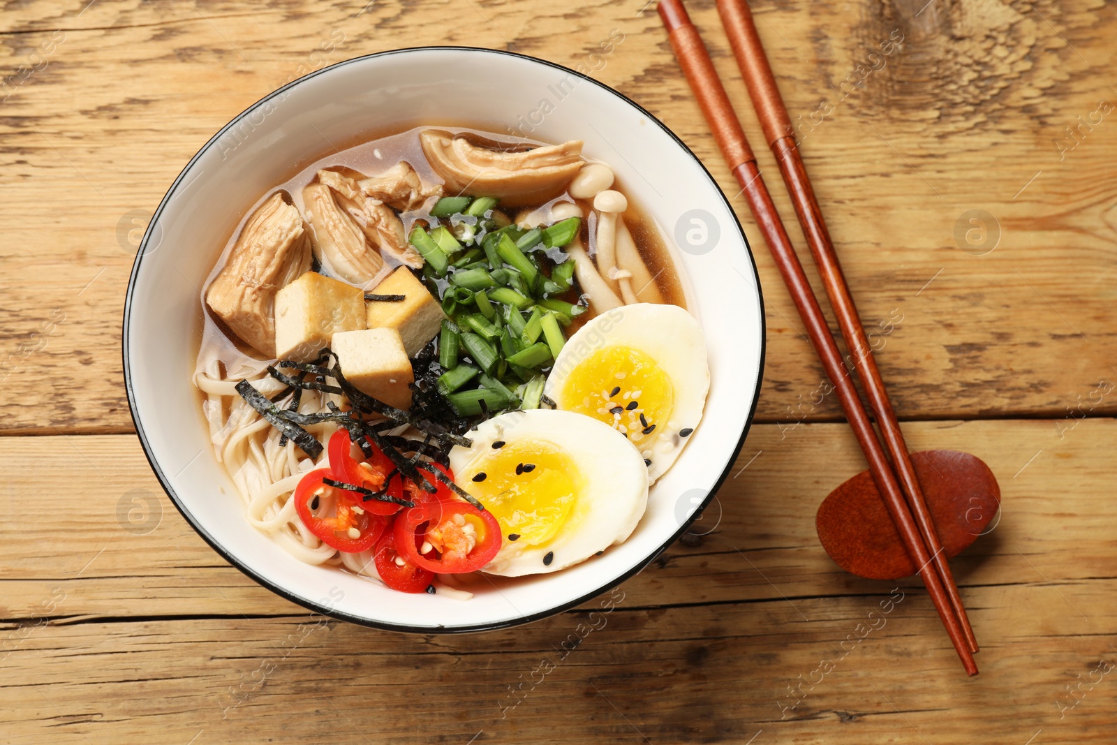 Photo of Noodle soup. Bowl of delicious ramen and chopsticks on wooden table, top view