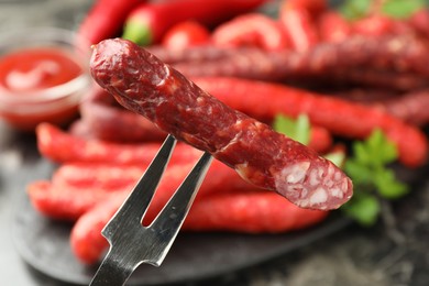 Photo of Fork with thin dry smoked sausage over table, closeup
