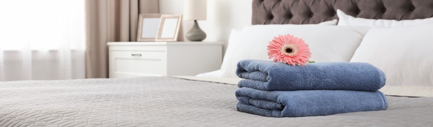 Image of Folded blue towels with pink gerbera on bed indoors, space for text. Banner design