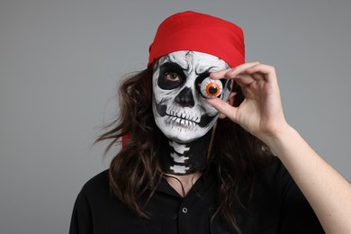 Photo of Man in scary pirate costume with skull makeup and decorative eyeball on light grey background. Halloween celebration