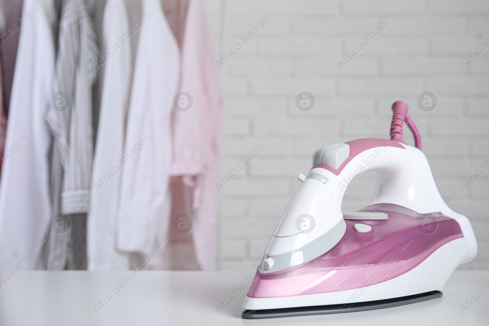 Photo of Modern iron on table near rack with clean clothes indoors, space for text