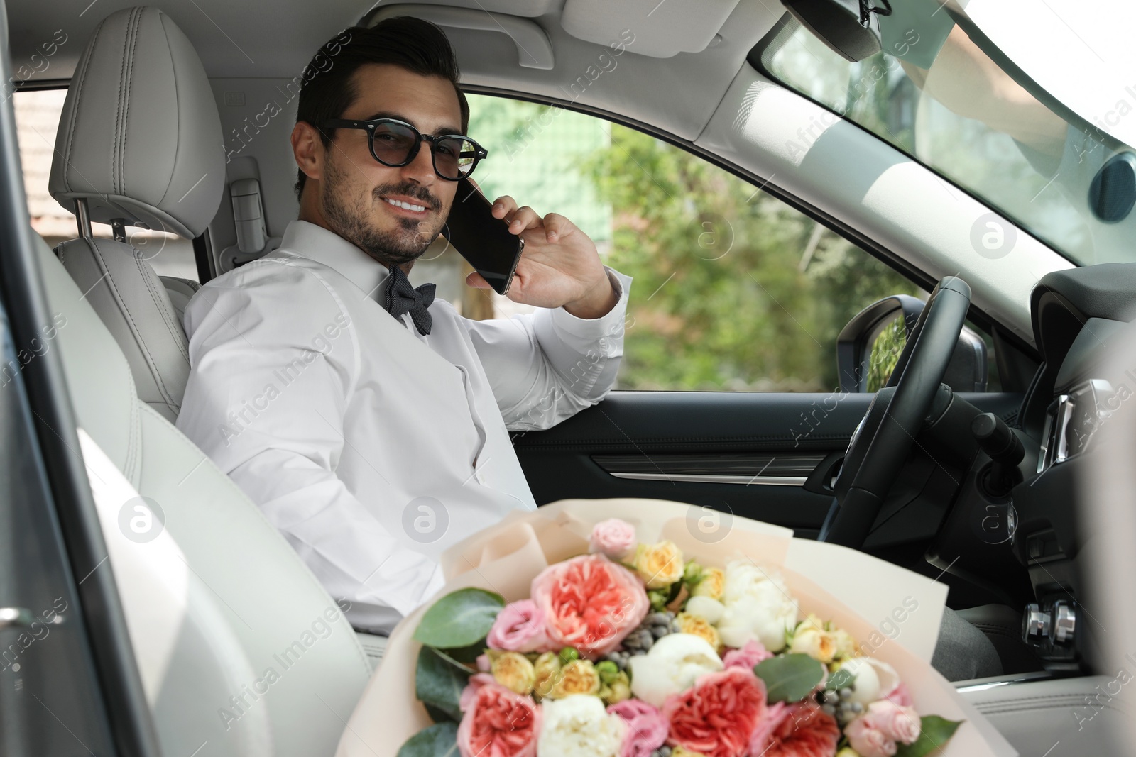 Photo of Young handsome man with beautiful flower bouquet sitting in car