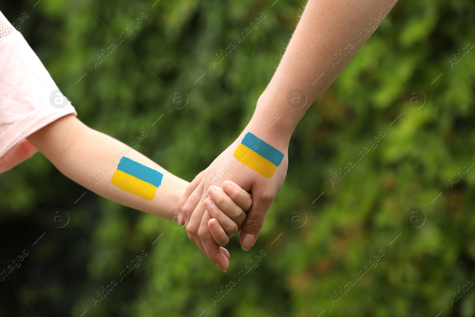 Image of Help for Ukraine. Woman and child holding hands with drawings of Ukrainian flag outdoors, closeup