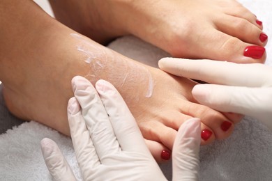 Photo of Pedicurist applying cream onto client`s foot after pedicure procedure in beauty salon, closeup