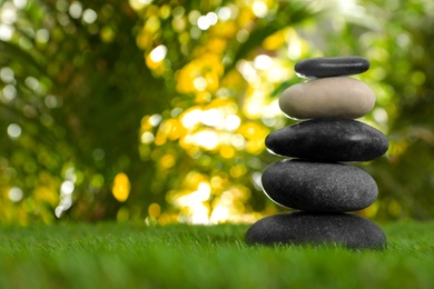 Photo of Stack of stones on green grass against blurred background, space for text. Zen concept