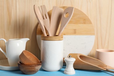 Set of different kitchen utensils on light blue table against wooden background
