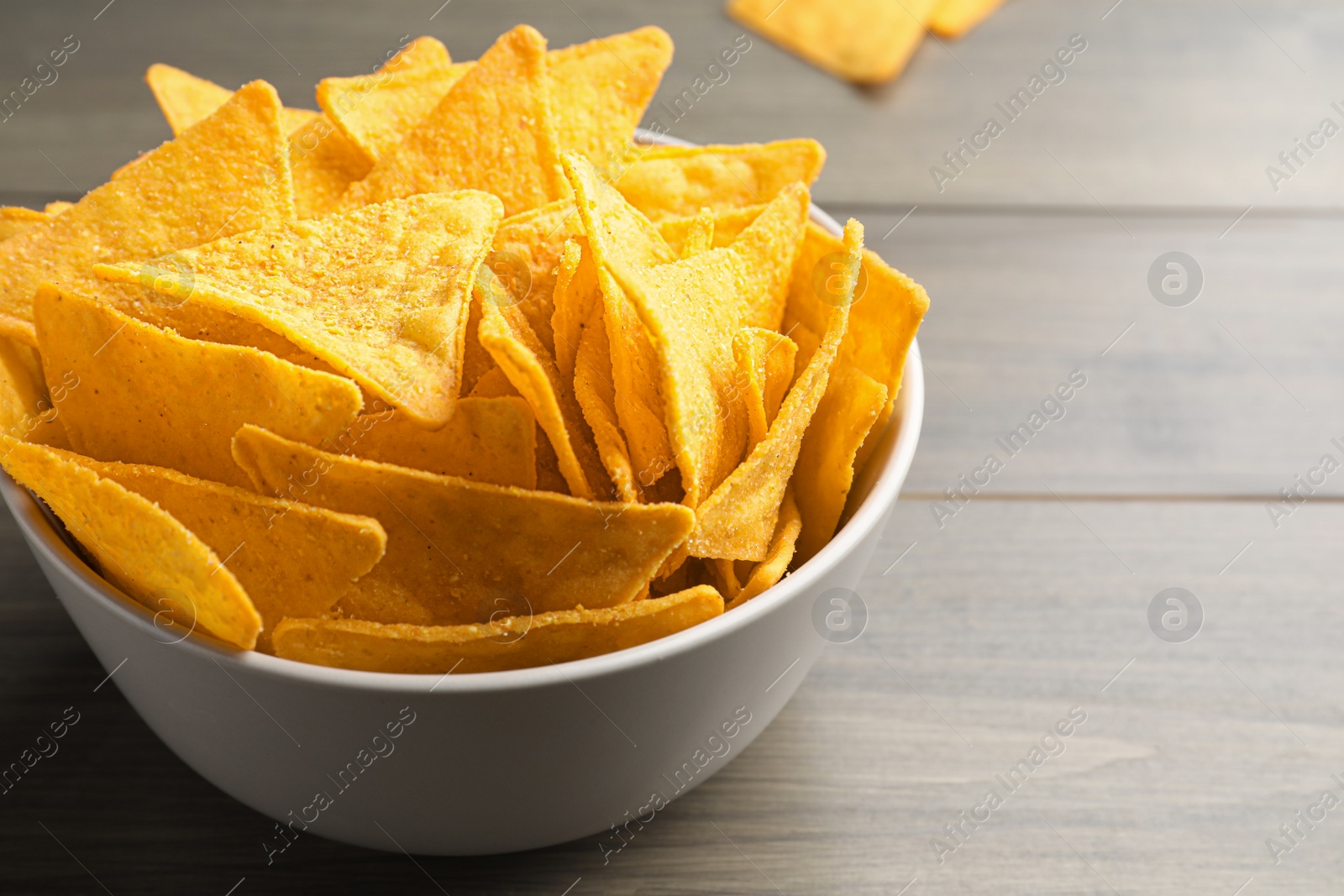 Photo of Tortilla chips (nachos) in bowl on wooden table, closeup