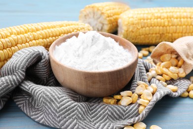 Photo of Bowl with corn starch, ripe cobs and kernels on light blue wooden table