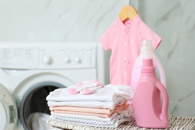 Photo of Bottles of detergent and children's clothes on wicker basket in bathroom