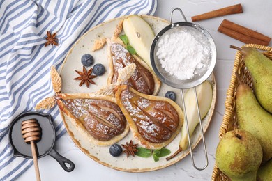 Delicious pears baked in puff pastry with powdered sugar served on white table, flat lay