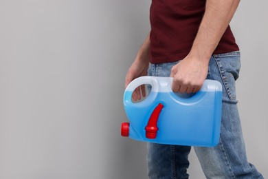 Photo of Man holding canister with blue liquid on light grey background, closeup. Space for text